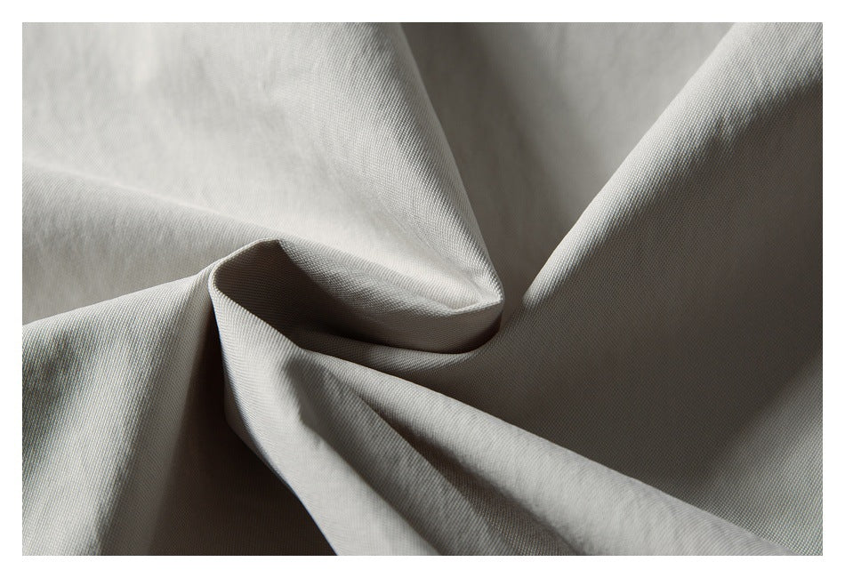 Close-up of light gray jacket fabric gathered into folds, showing its surface texture.