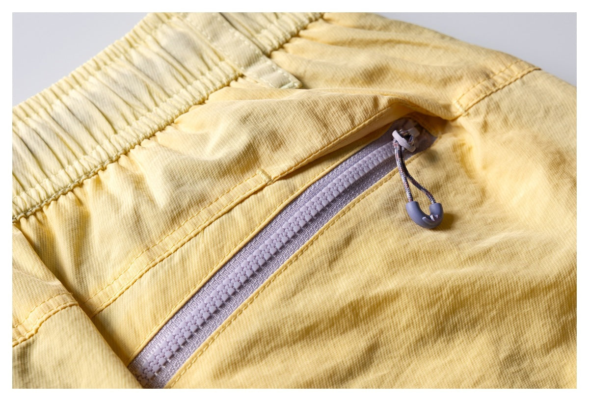 Close-up of a lavender zip pocket and drawcord pull on pale yellow patterned shorts.