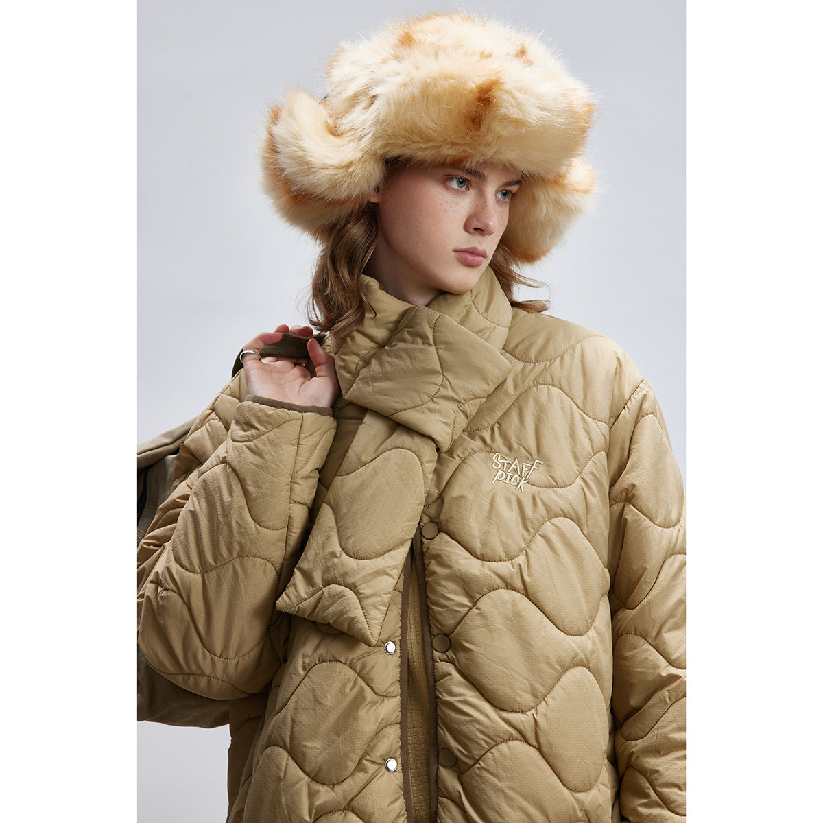 Model wearing a tan wave-quilted jacket with a padded wrap collar and snap buttons, shown from the front.