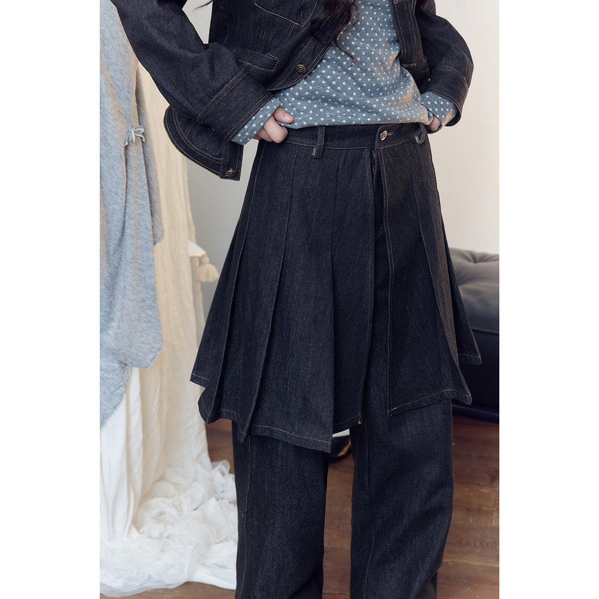 Close view of a model wearing dark denim wide-leg trousers with a pleated skirt overlay and a polka-dot top.