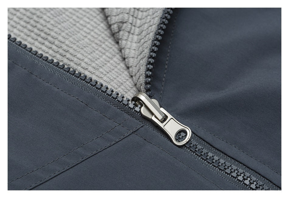 Close-up of a dark zipper and metal pull joining charcoal fabric with a light gray textured panel.