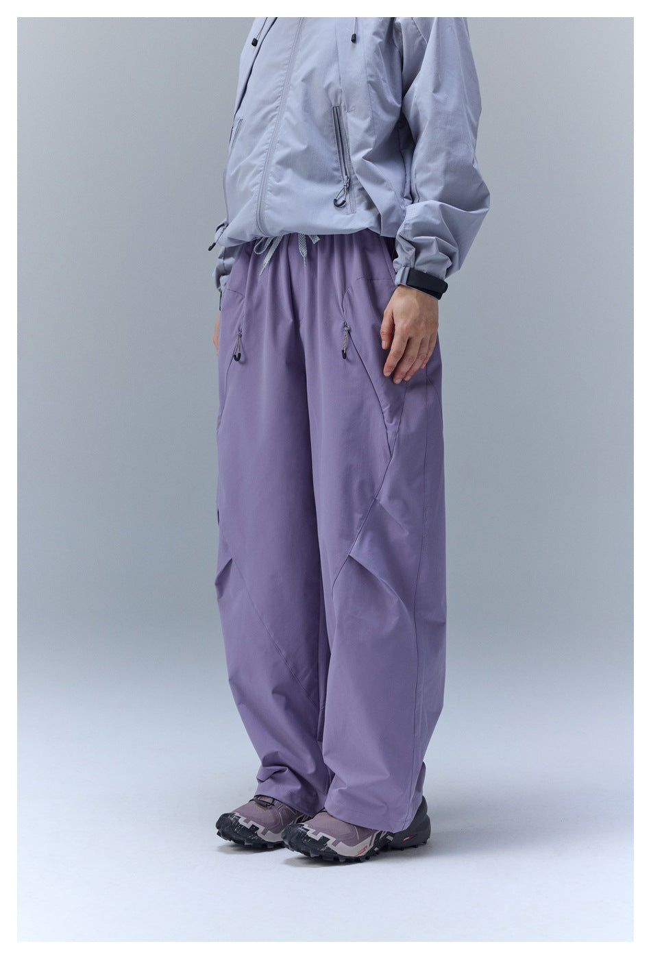 Cropped view of a person wearing loose lavender-purple pants with an elastic waist, drawcord, and zip pockets.