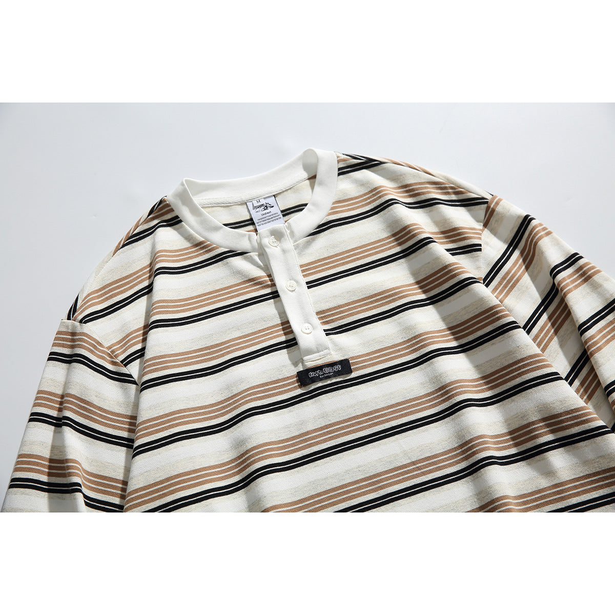 Close-up of an ivory long-sleeve shirt with tan and black horizontal stripes, a white collar, and a three-button placket.