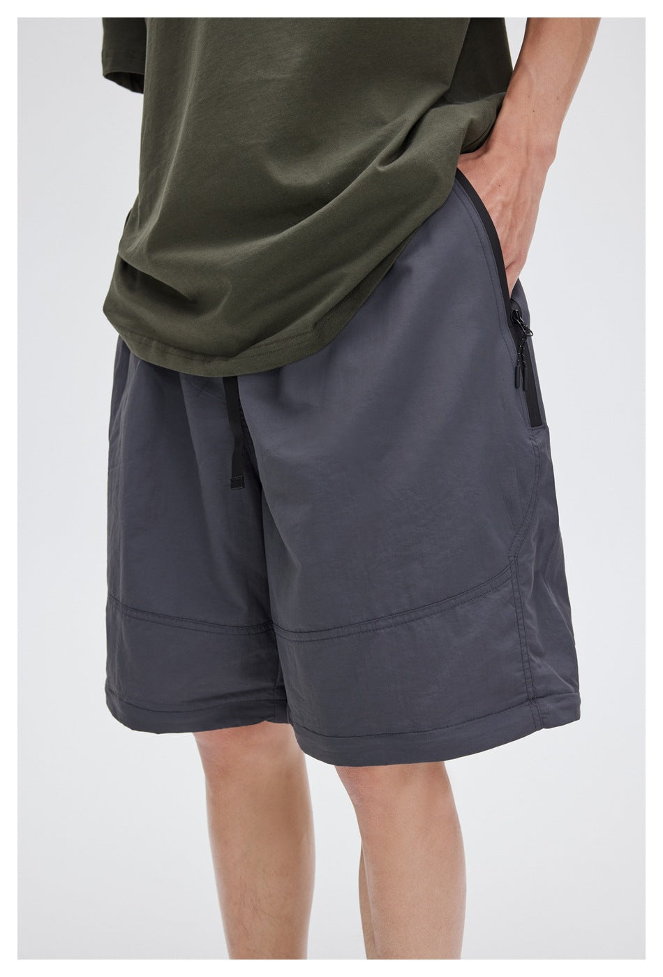 Close angled view of slate-gray shorts on a model, showing a black zip pocket and panel seams.