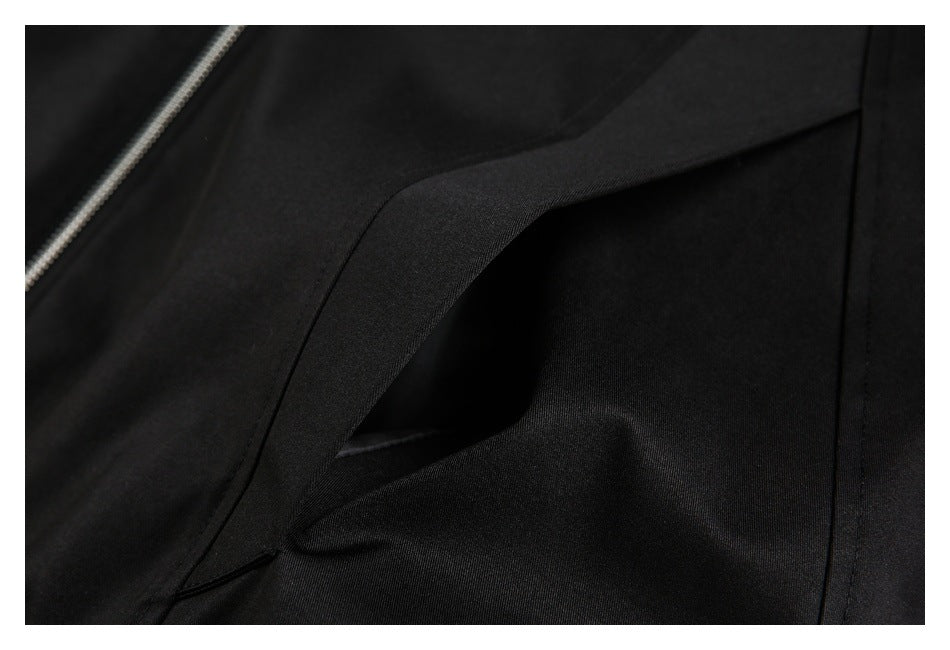 Close-up of a slanted pocket opening on black jacket fabric, with part of the silver zipper visible.