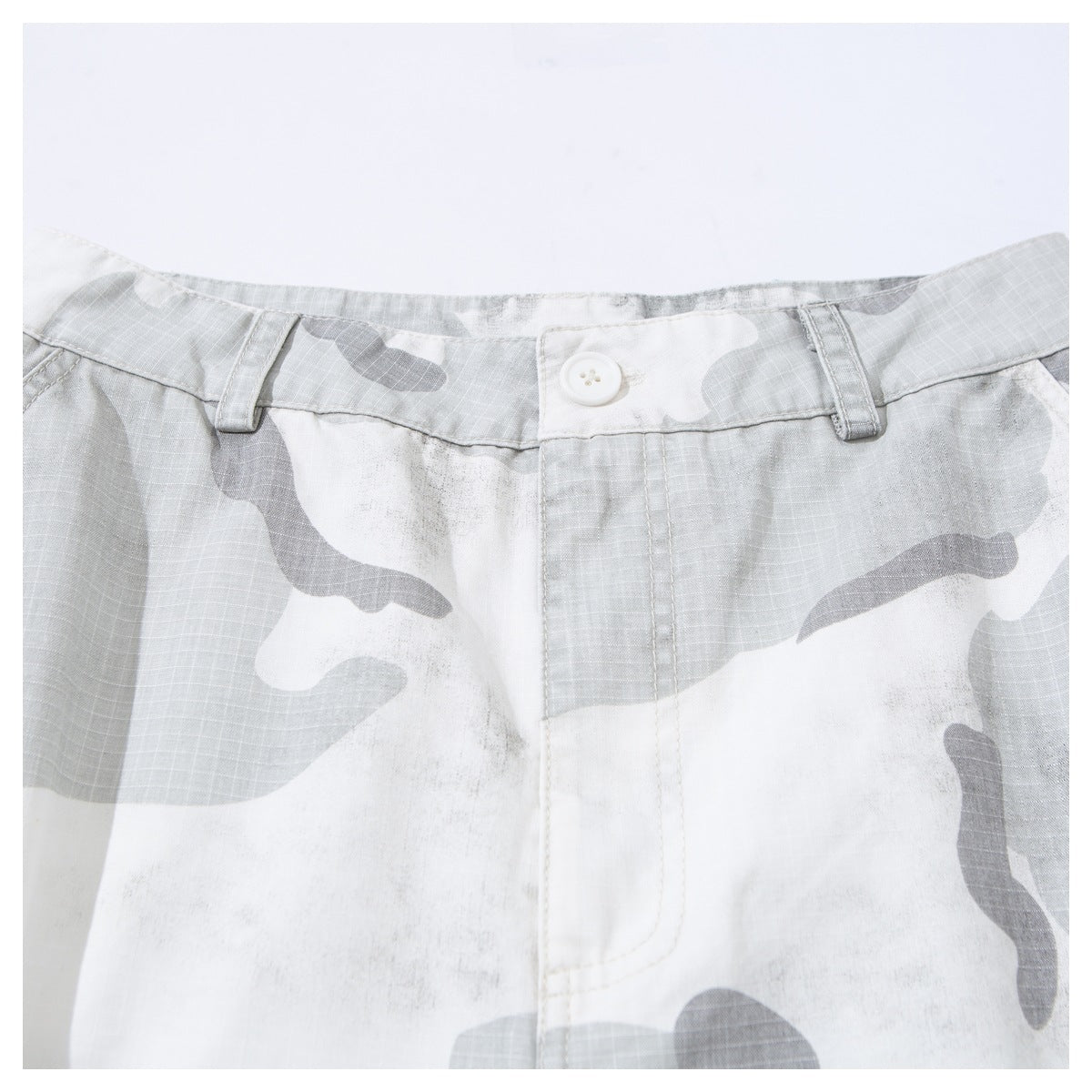 Close-up of the buttoned waistband and fly on gray and white camouflage shorts.