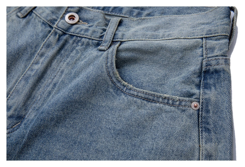 Close-up of light blue washed jeans showing the front pocket, waistband button, belt loop and rivet.