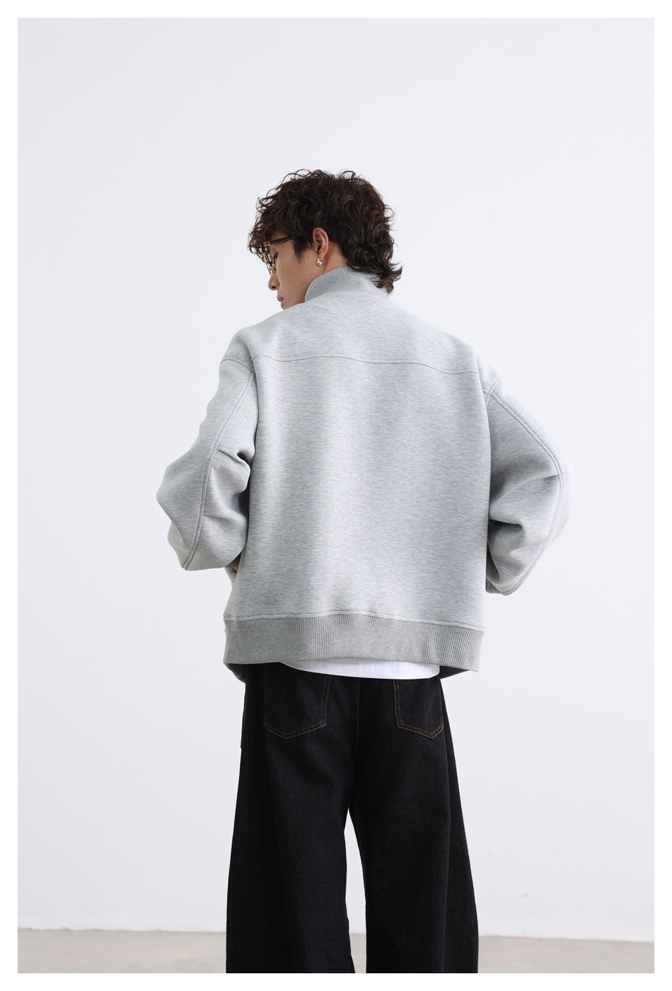 Rear view of a model wearing a light gray jacket with a high collar, dropped shoulders, and ribbed hem.