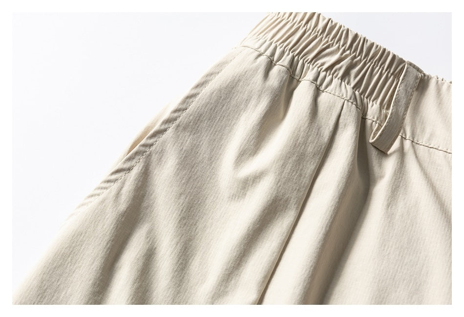 Close-up of light beige trousers showing the elastic waistband, belt loop, and front pocket seam.
