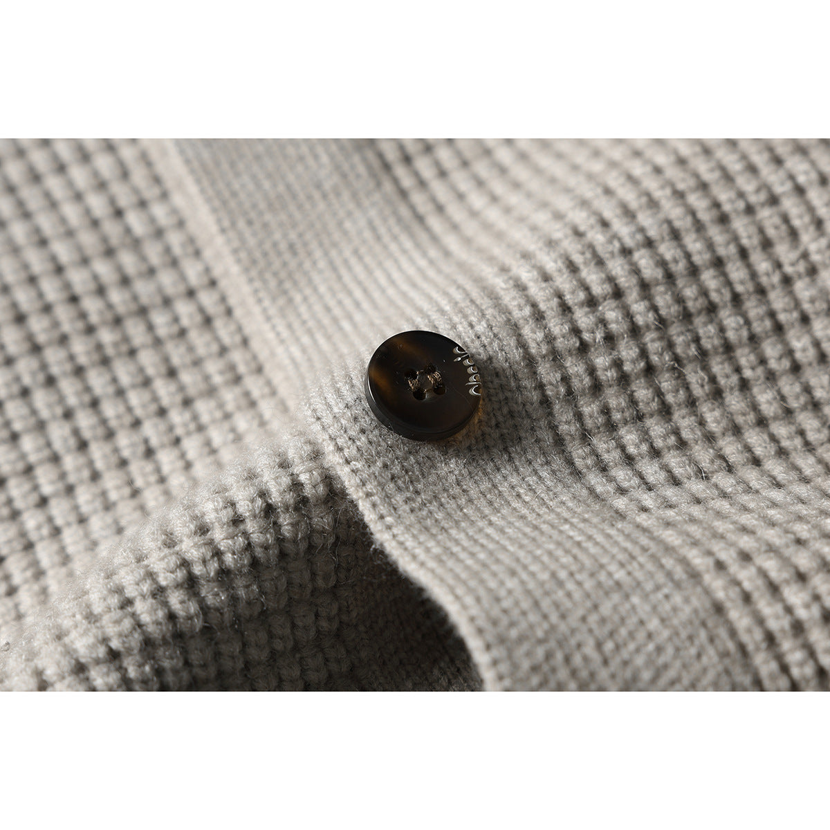 Close-up of a dark four-hole button on the textured light gray knit cardigan.