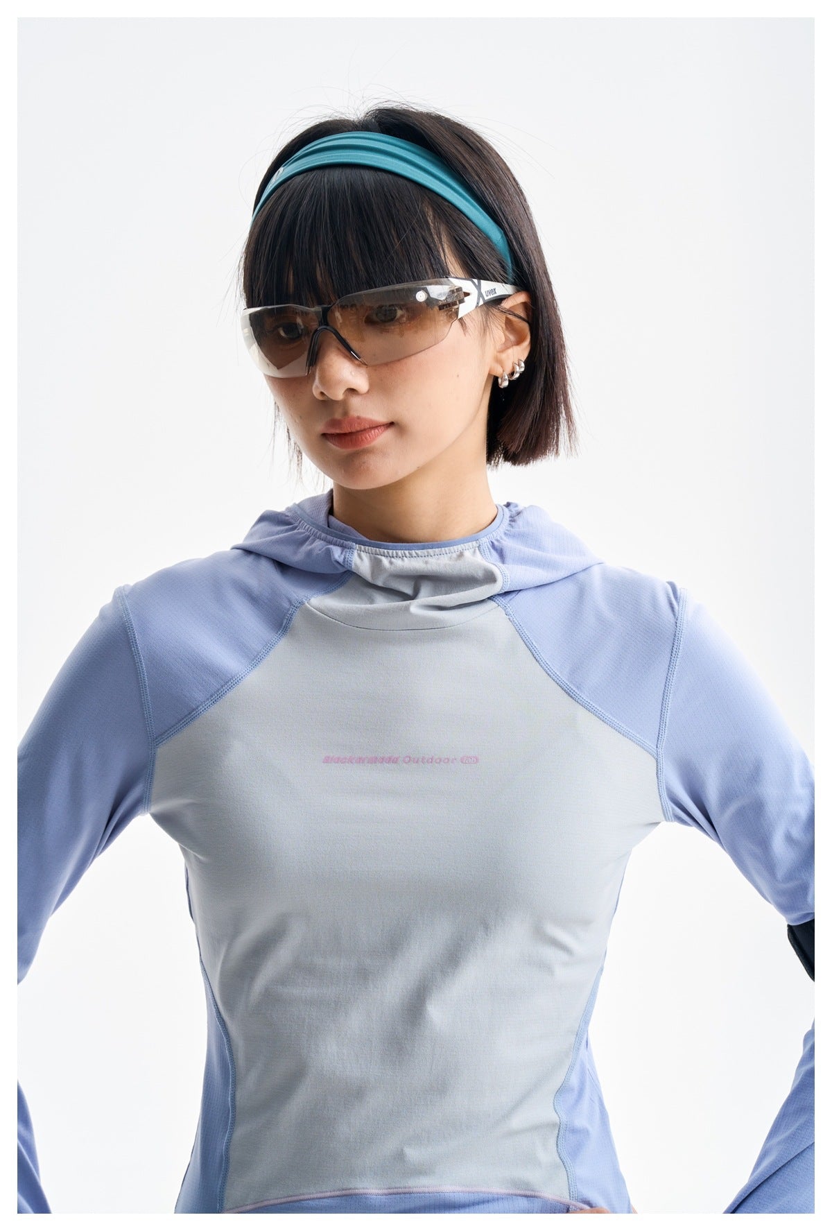 Close-up of a model wearing a light blue and pale gray hooded top with small pink chest lettering.