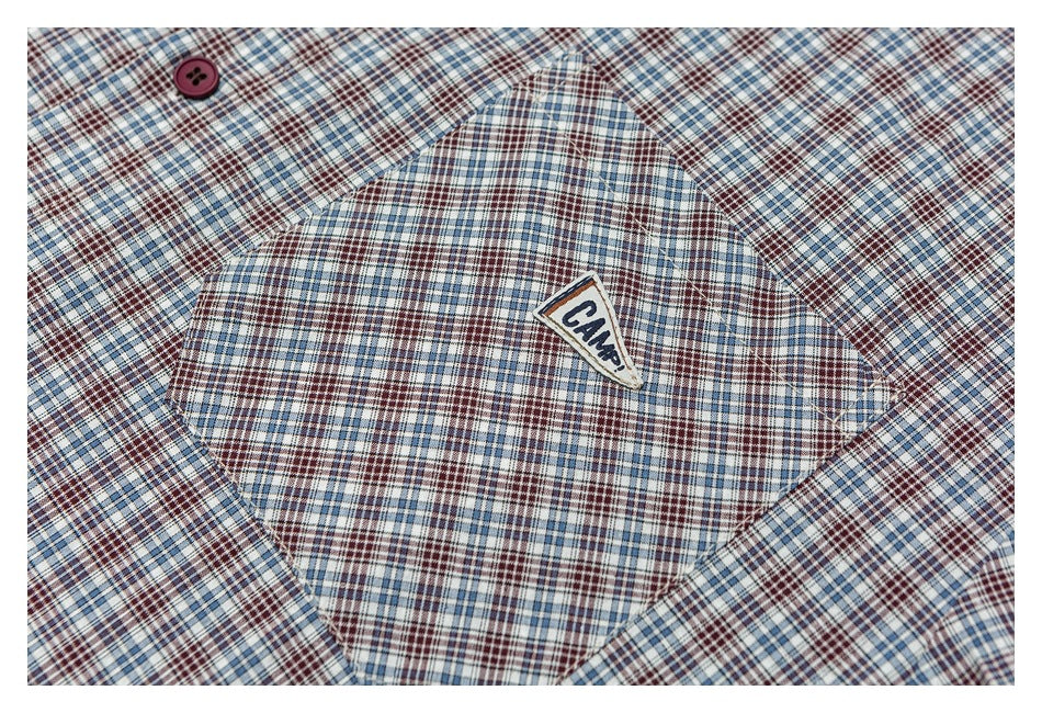 Close-up of a plaid garment pocket with a burgundy button and a sewn CAMP label.