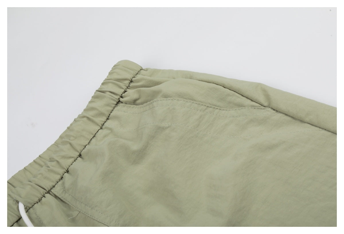 Close-up of the sage-green shorts' elastic waistband and curved stitched pocket detail.