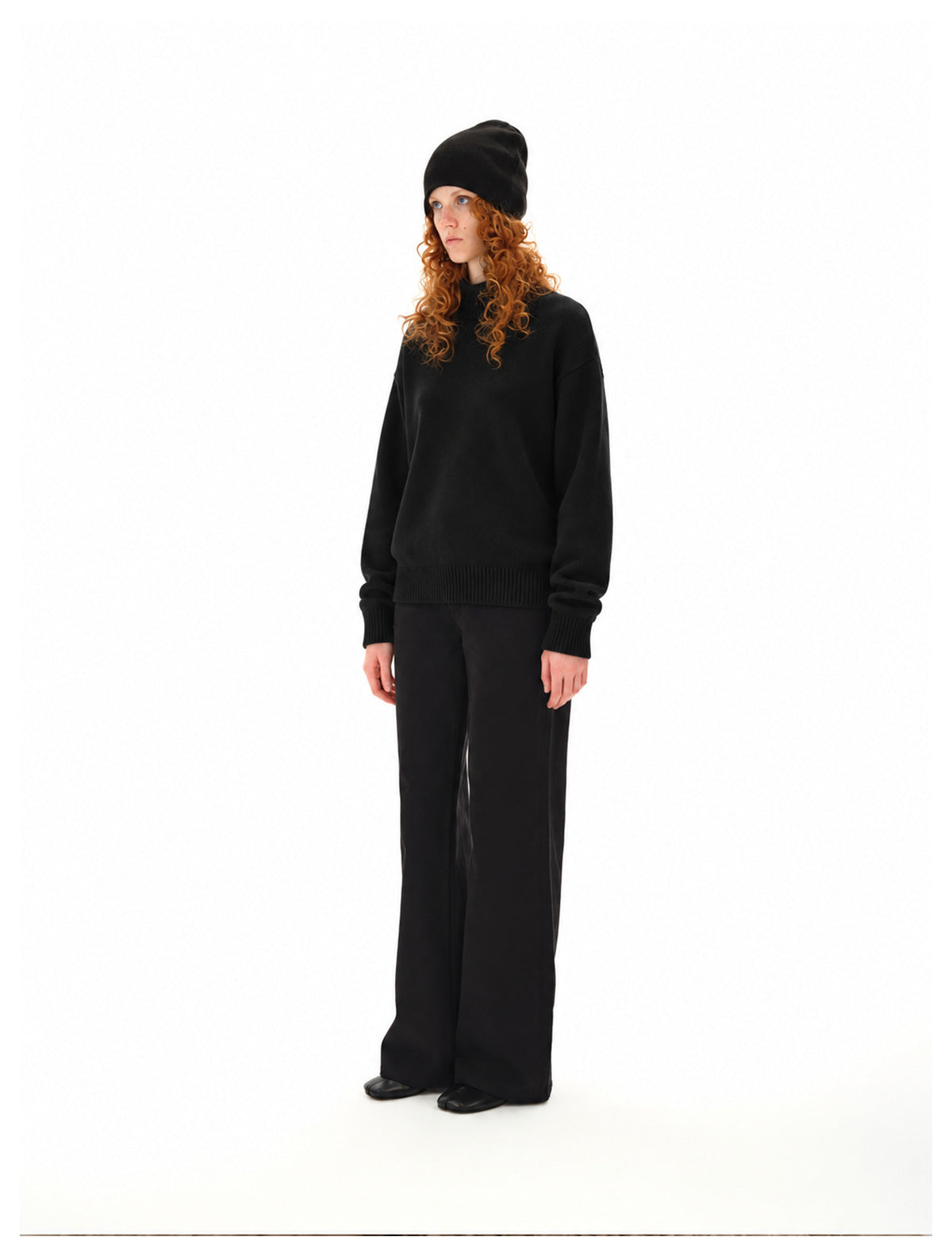 Woman wearing a black high-neck sweater with ribbed cuffs and hem, black trousers and a black beanie.