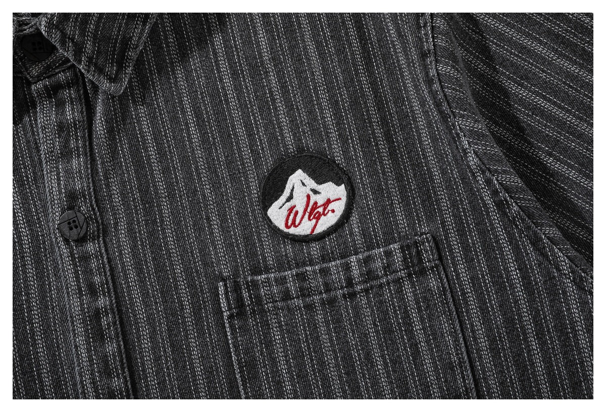 Closer view of the shirt's embroidered chest patch and pocket on charcoal pinstriped fabric.