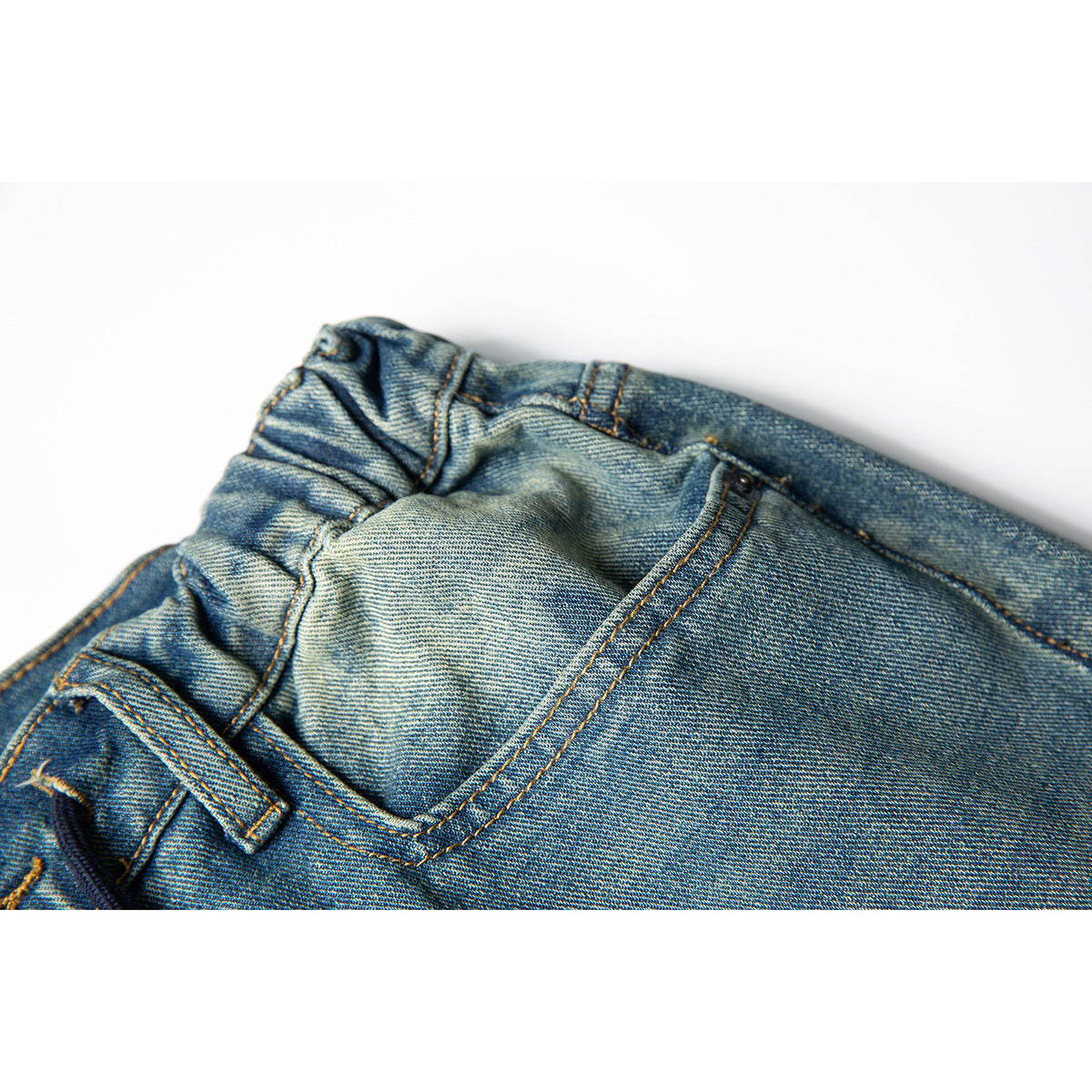 Close-up of the back waist and pocket area of faded blue denim trousers, showing seams and belt loops.