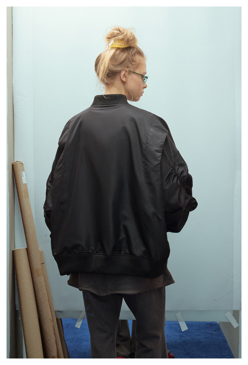 Back view of a model wearing an oversized black bomber jacket with a plain back and ribbed collar and hem.