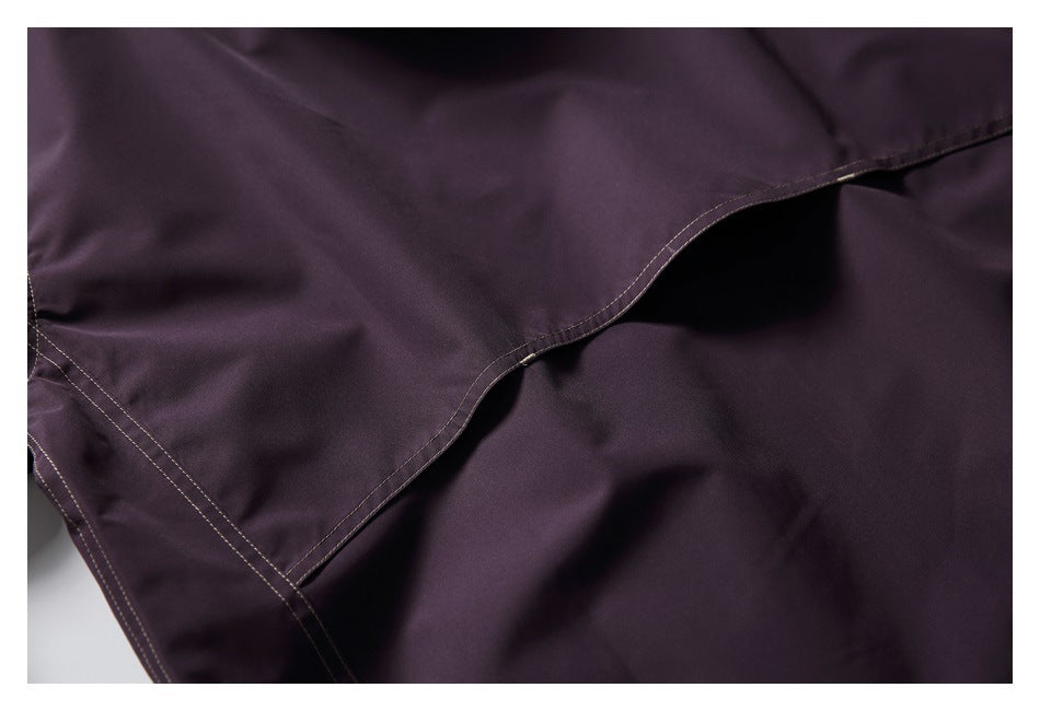 Close-up of a curved pocket opening and stitched panels on a dark plum garment.