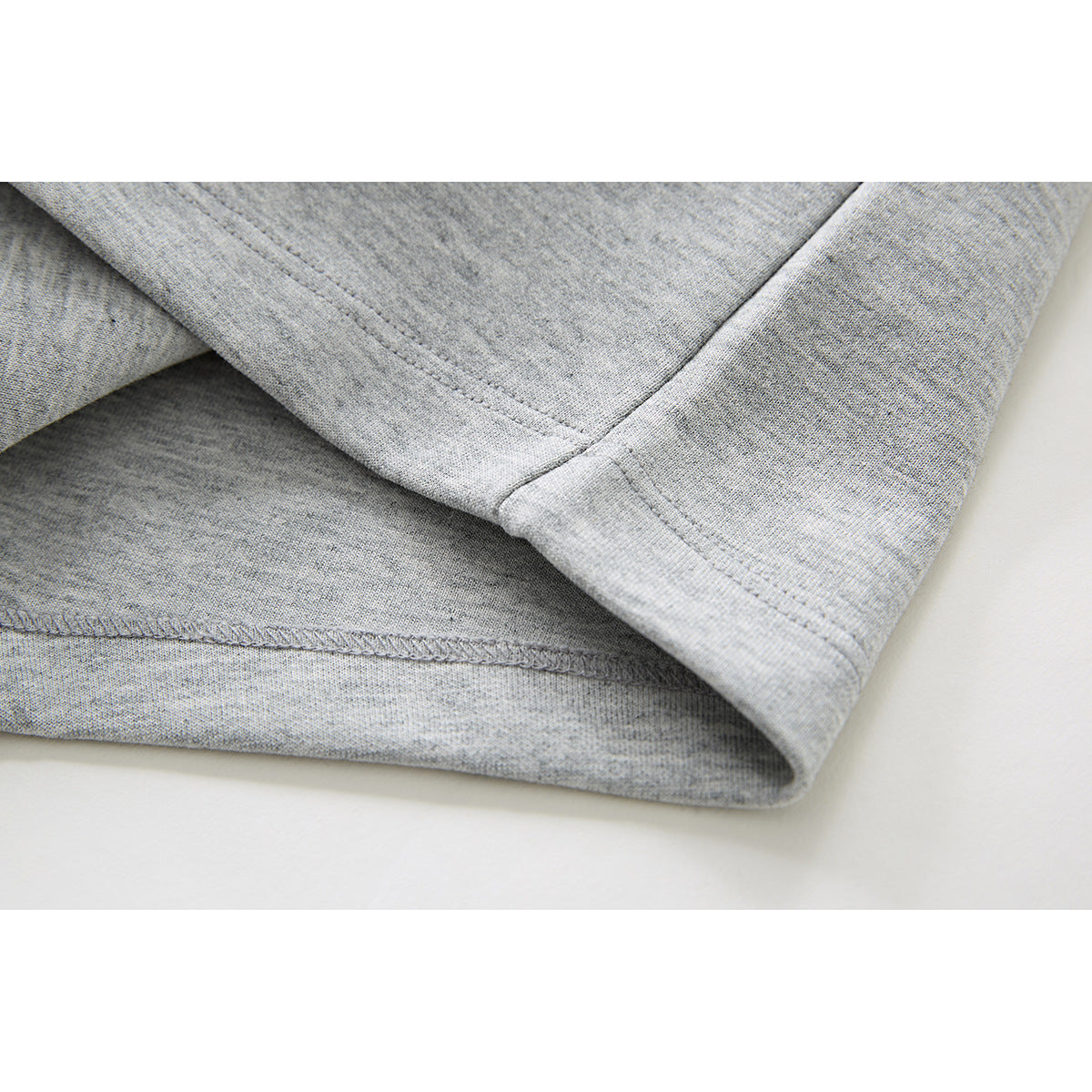 Close-up of the stitched hem and folded edge of light gray shorts.