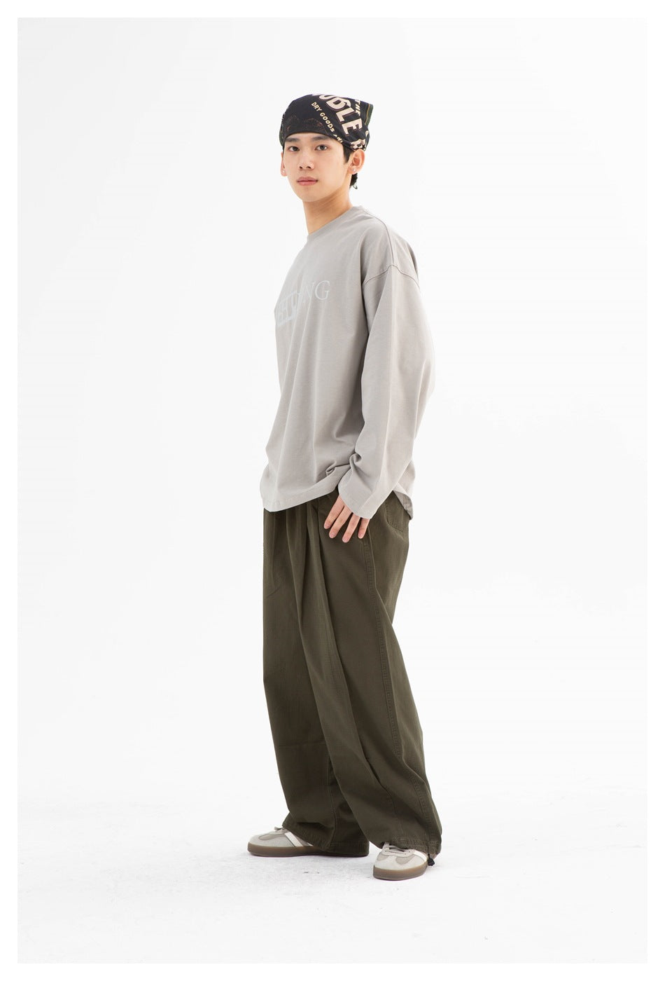 Full-length model in a gray oversized long-sleeve shirt with pale lettering and loose dark olive trousers.