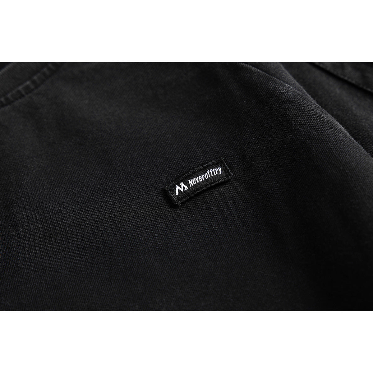 Close-up of a small black-and-white sewn logo patch on black T-shirt fabric.