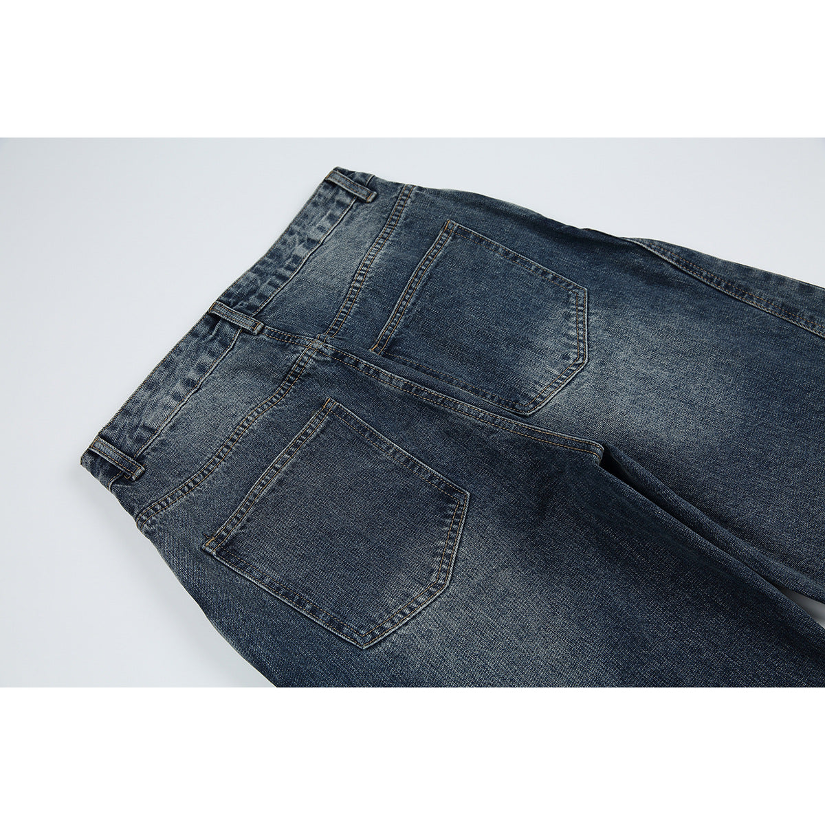 Close-up of the back of dark blue washed jeans, showing two patch pockets and belt loops.
