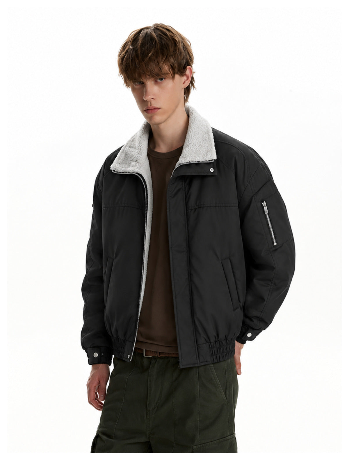 Model wearing an open black jacket with a white fleece collar, over a brown shirt and olive cargo pants.