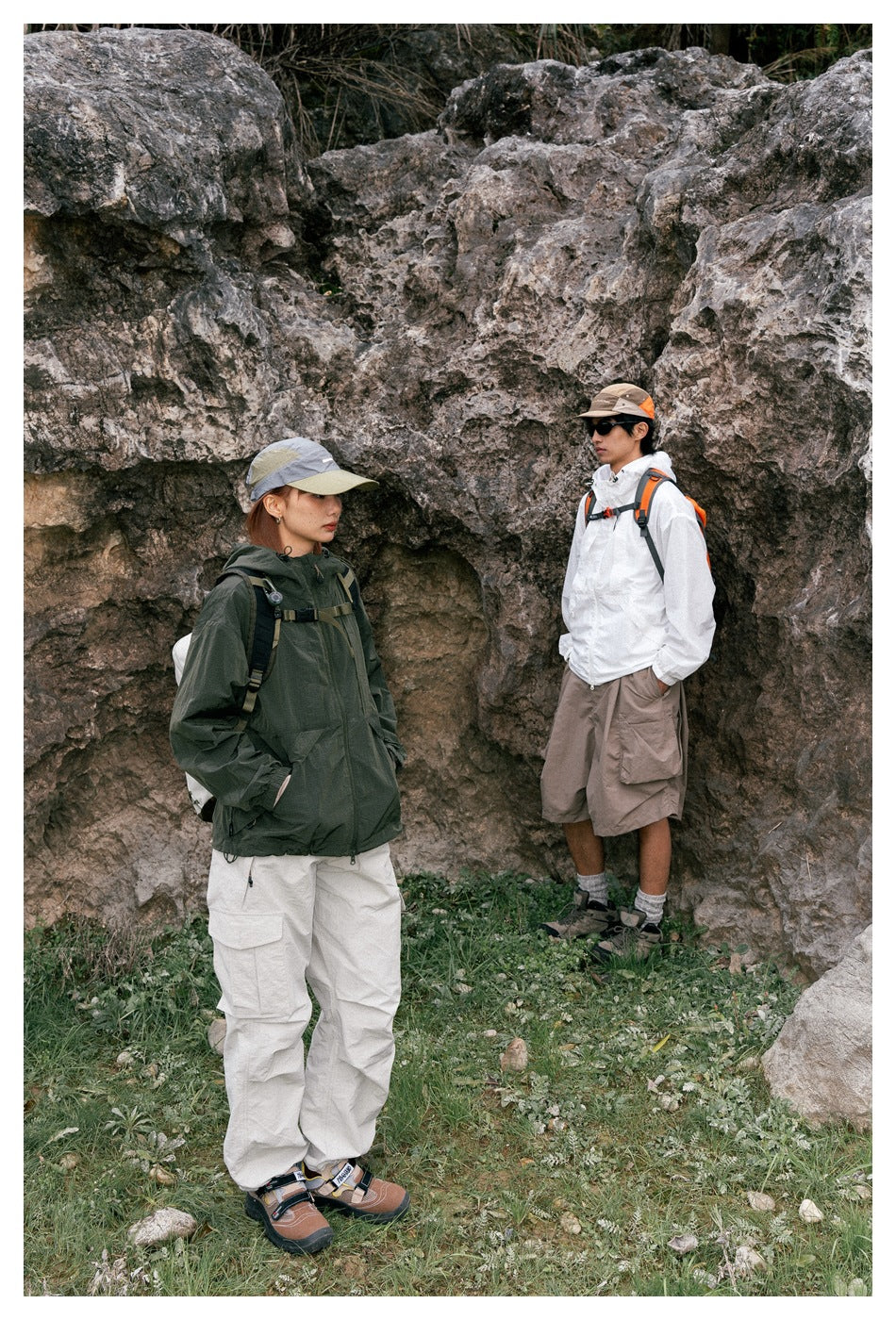 Two people outdoors by a rock face, one wearing a green hooded jacket and the other a white jacket
