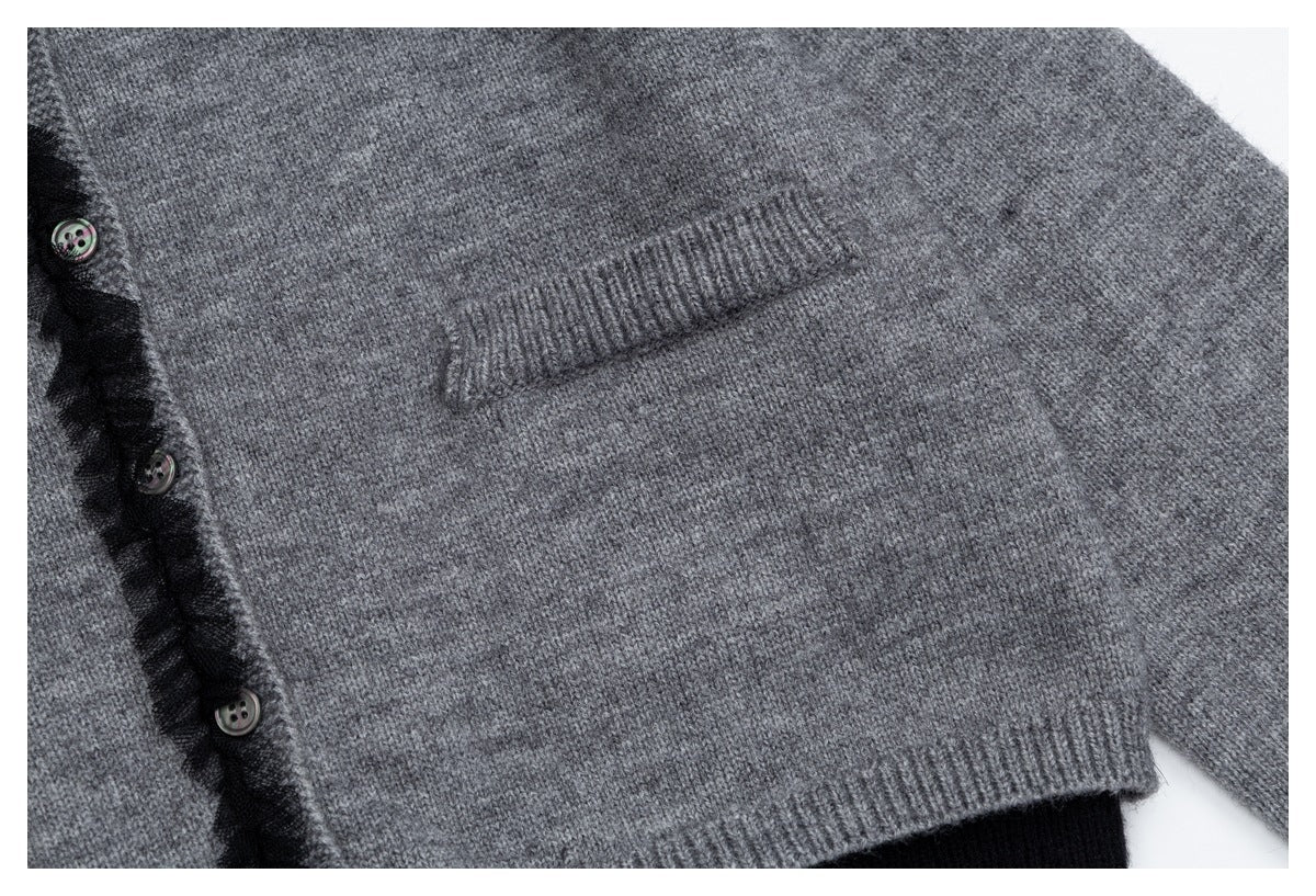 Close-up of a gray knit cardigan showing a ribbed front pocket, black ruffle trim, buttons, and ribbed hem.