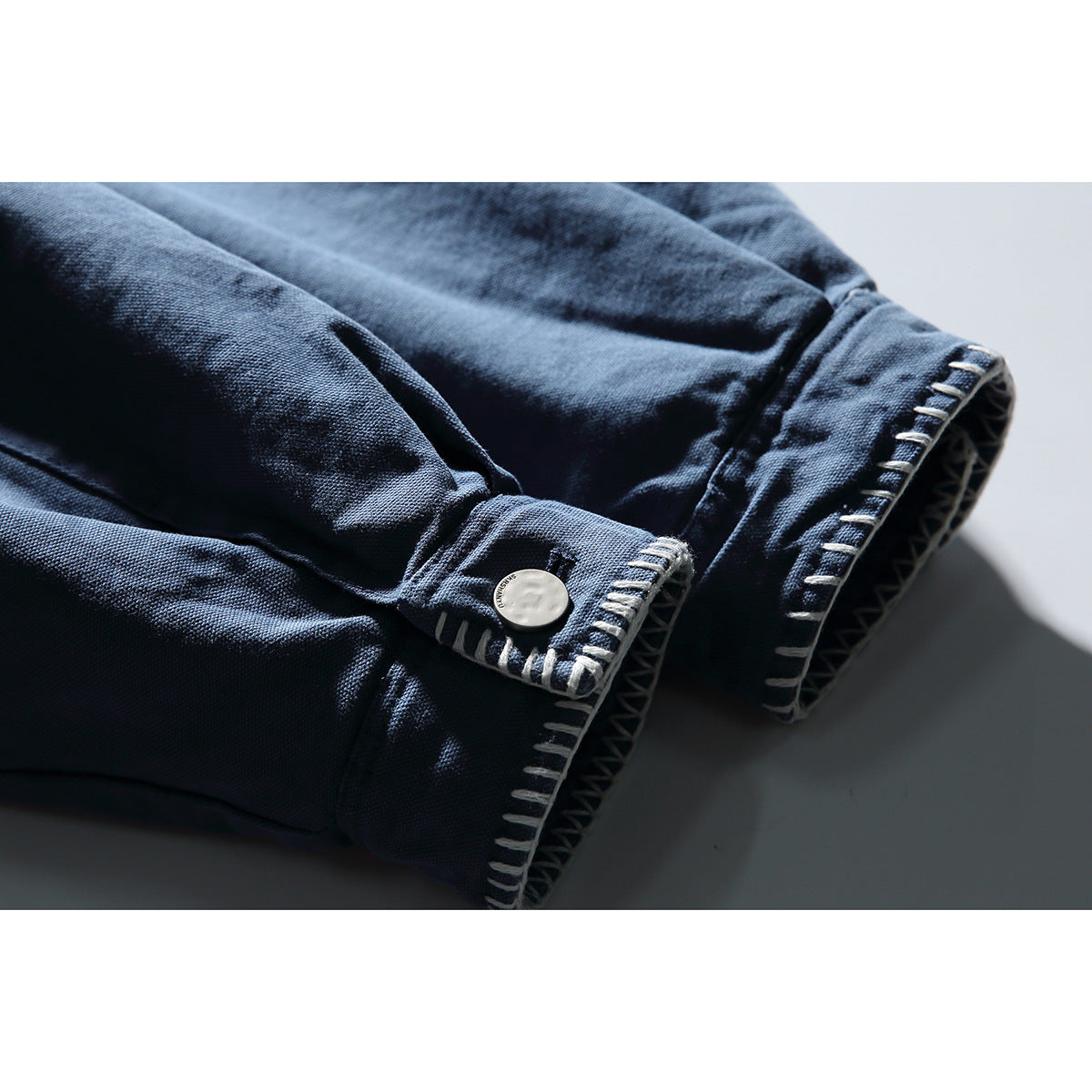 Close-up of blue jacket cuffs with white contrast stitching and a round metal button.