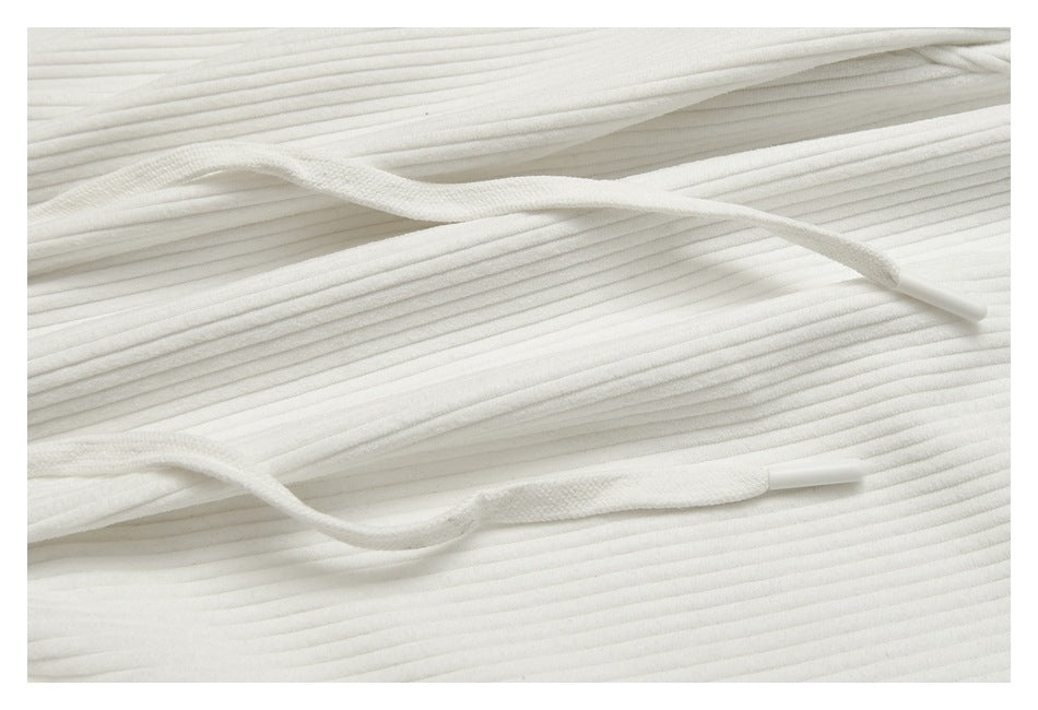 Close-up of white drawstrings and their plastic tips lying across ribbed white pants.