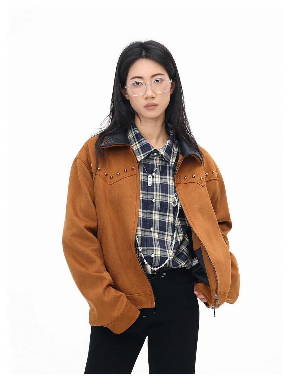 Waist-up view of a model in a rust-brown studded jacket over a navy plaid shirt and black trousers.