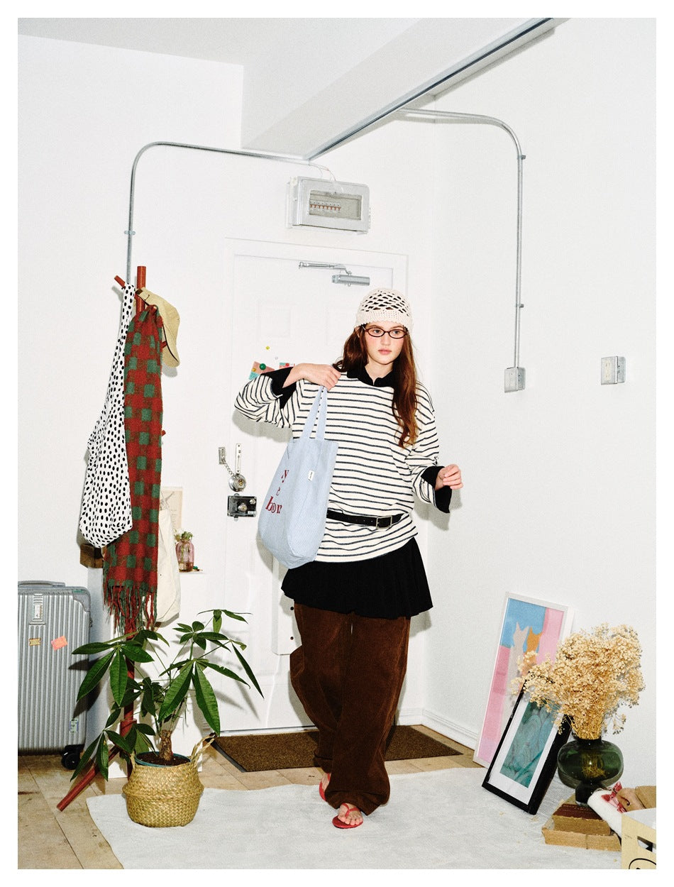 Model wearing an oversized cream-and-dark striped shirt with black cuffs, a black skirt, and loose brown trousers.