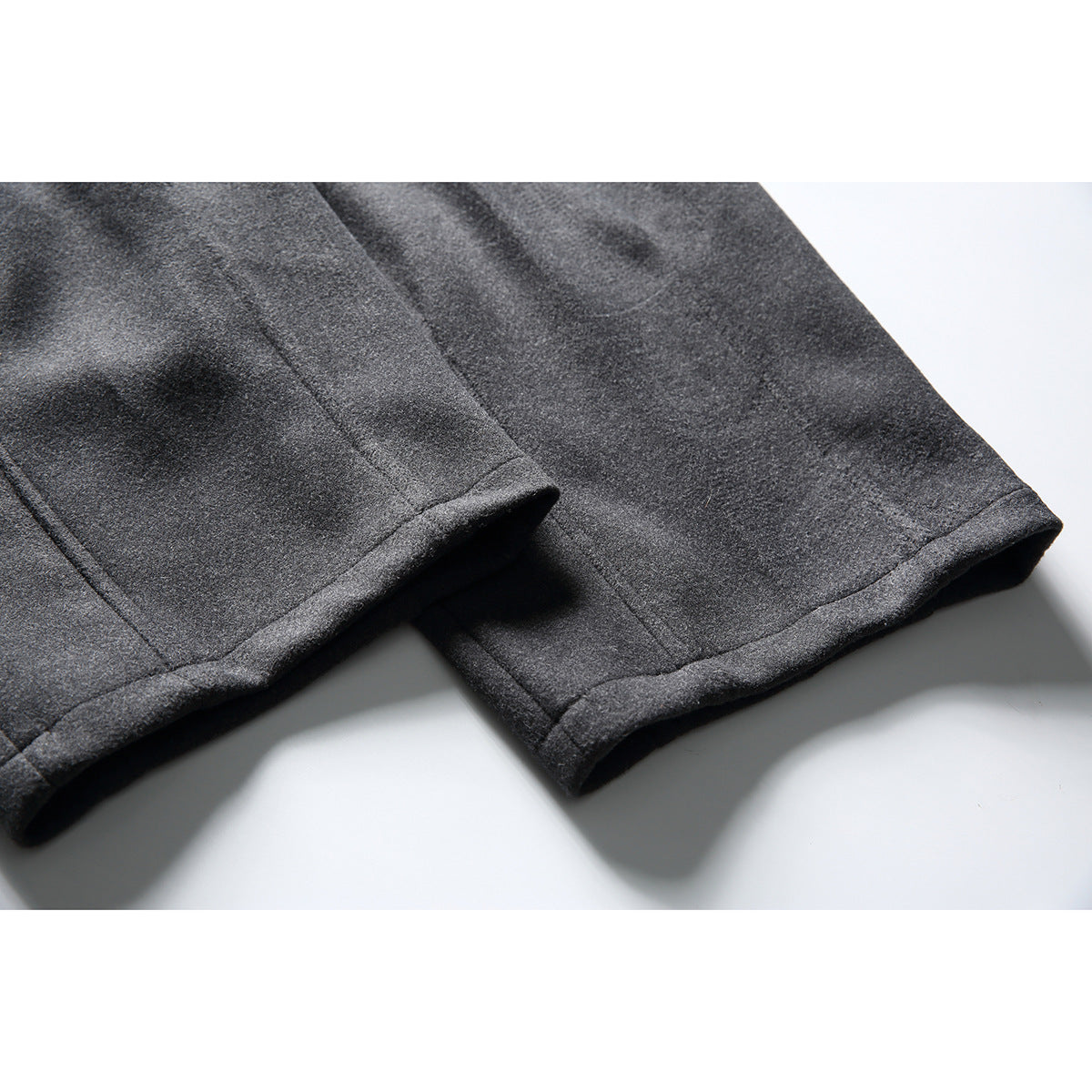 Close-up of charcoal trouser leg hems, showing folded edges and stitching.