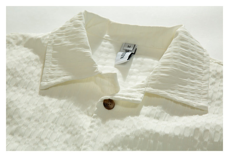 Close-up of an ivory textured shirt collar, neckline label, and brown button.