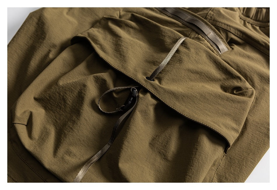 Close-up of olive-brown trousers with a flap pocket and adjustable drawcord detail.