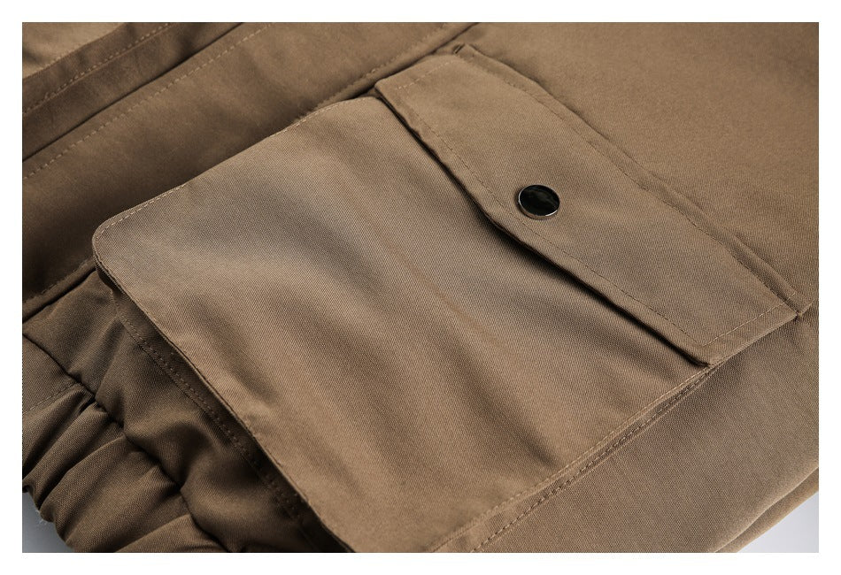 Close-up of a brown garment with a large flap pocket, black snap button, and gathered edge.