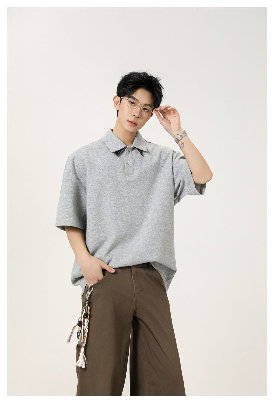Model wearing an oversized light gray short-sleeve polo with a pointed collar and dark striped collar accents.