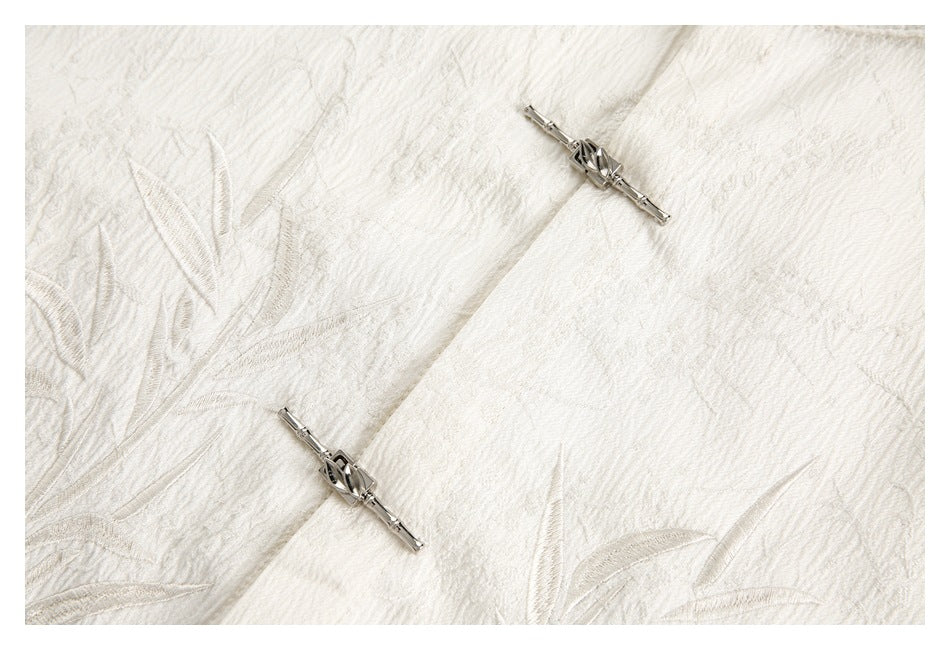 Close-up of ivory raised foliage embroidery with two silver frog-style fasteners.