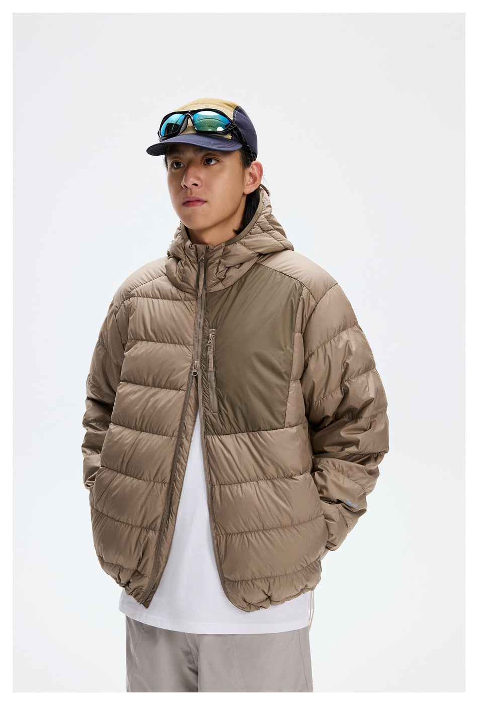 Man wearing a taupe hooded puffer jacket with a darker chest panel, shown from the front against a white studio background.