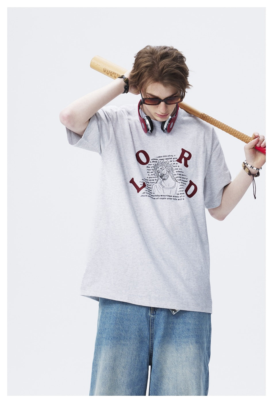 Close view of model in light gray graphic T-shirt with red LORD lettering, headphones and baseball bat