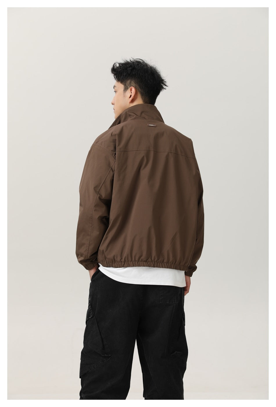Back view of a model wearing the brown stand-collar jacket with elastic hem and cuffs over a white tee