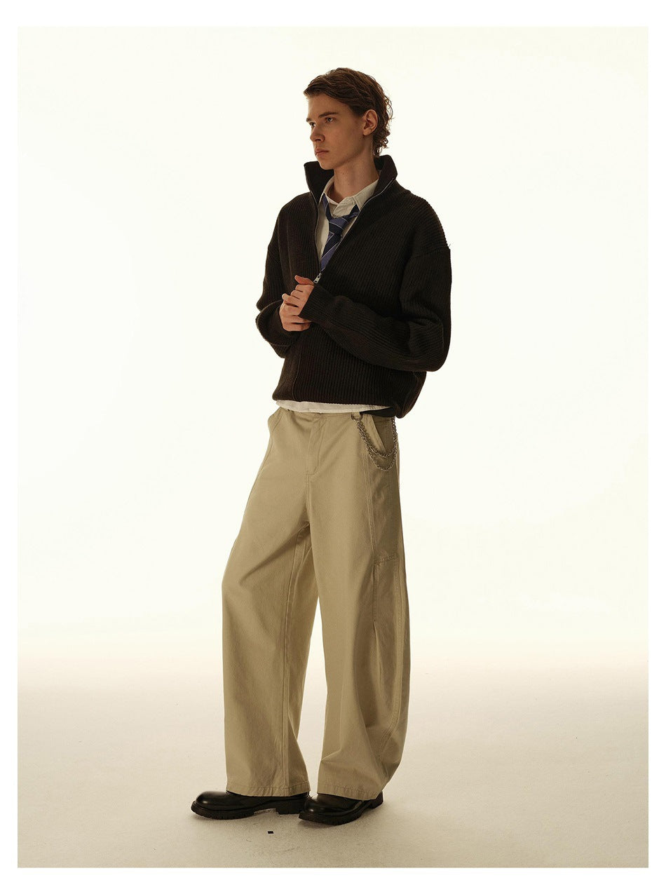 Full-length model in a dark ribbed zip-up cardigan, white shirt, striped tie, and loose beige trousers.