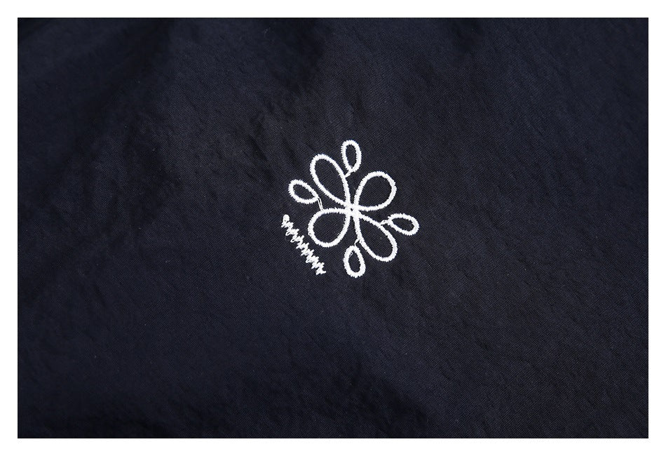 Close-up of a small white embroidered flower emblem on navy jacket fabric.
