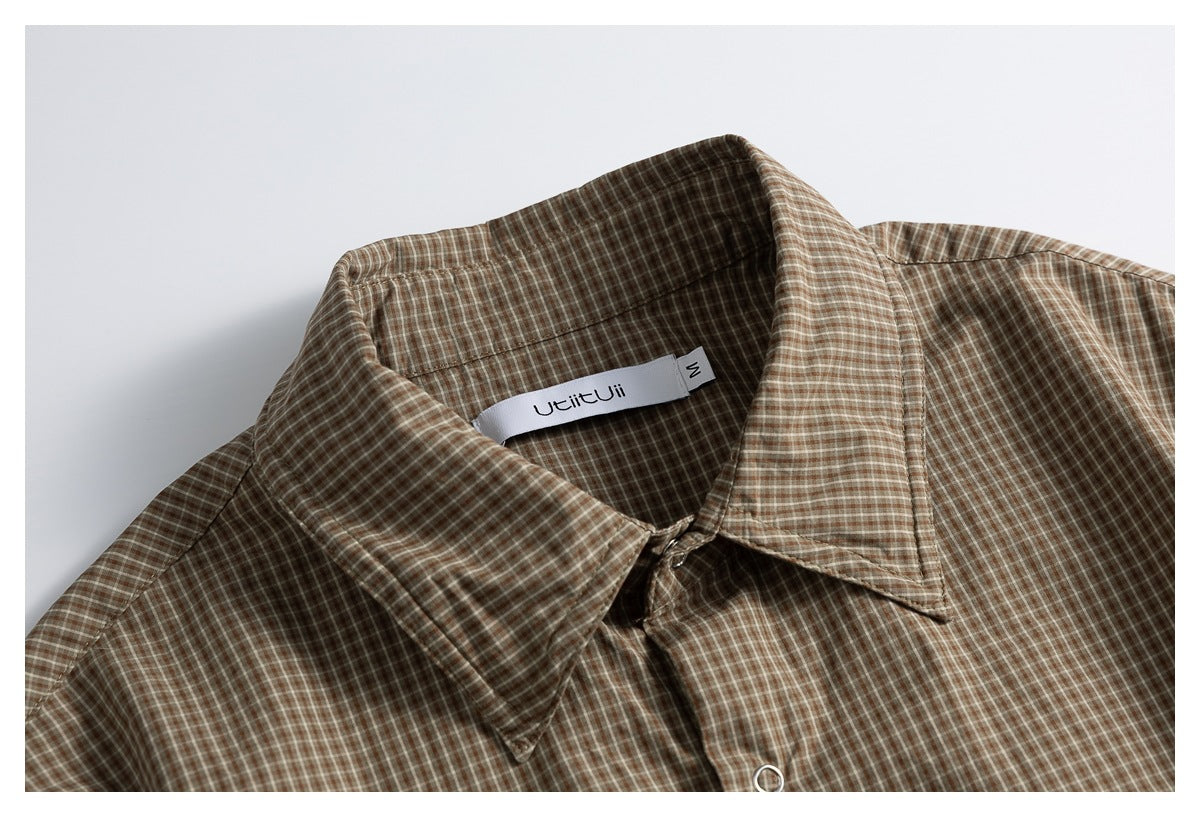 Close-up of a brown and beige checked shirt collar, with its sewn-in neck label and a metal button.