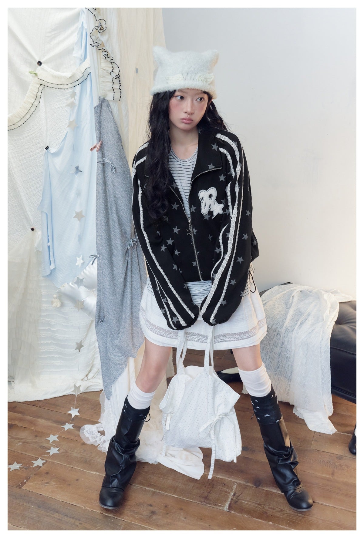 Model wearing a black zip jacket with gray stars, white lace sleeve stripes and a chest patch, paired with a striped top and