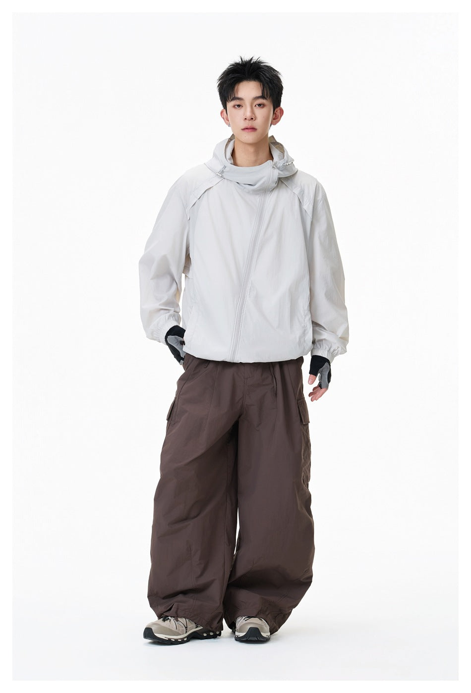 Model standing in a light gray-white hooded jacket with diagonal zipper and brown wide-leg cargo pants