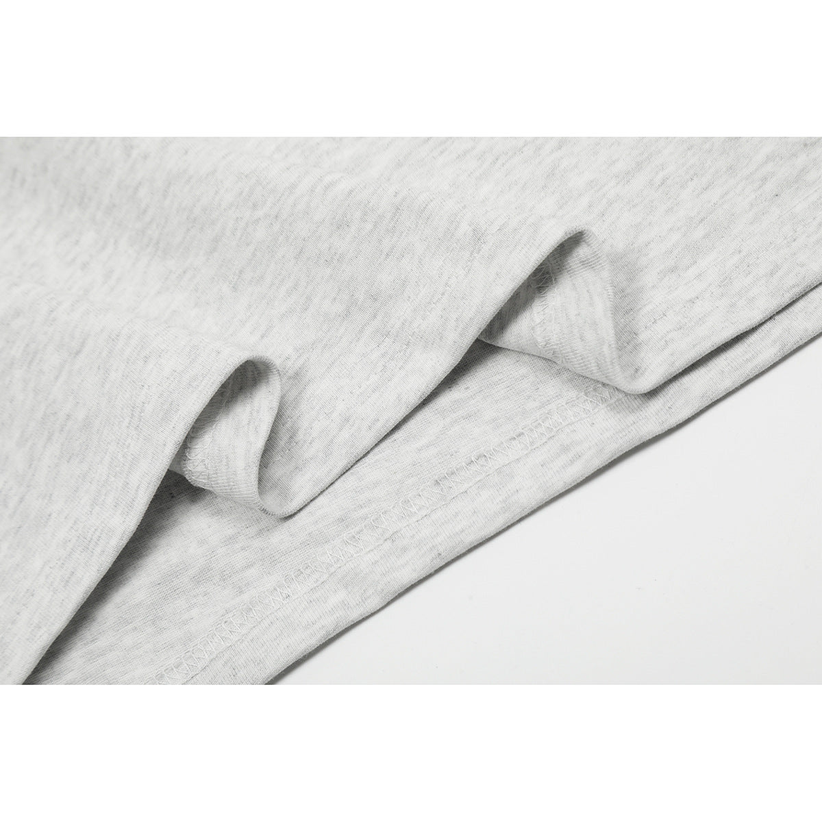 Close-up of the light gray heathered shirt's folded hem and overlock stitching.