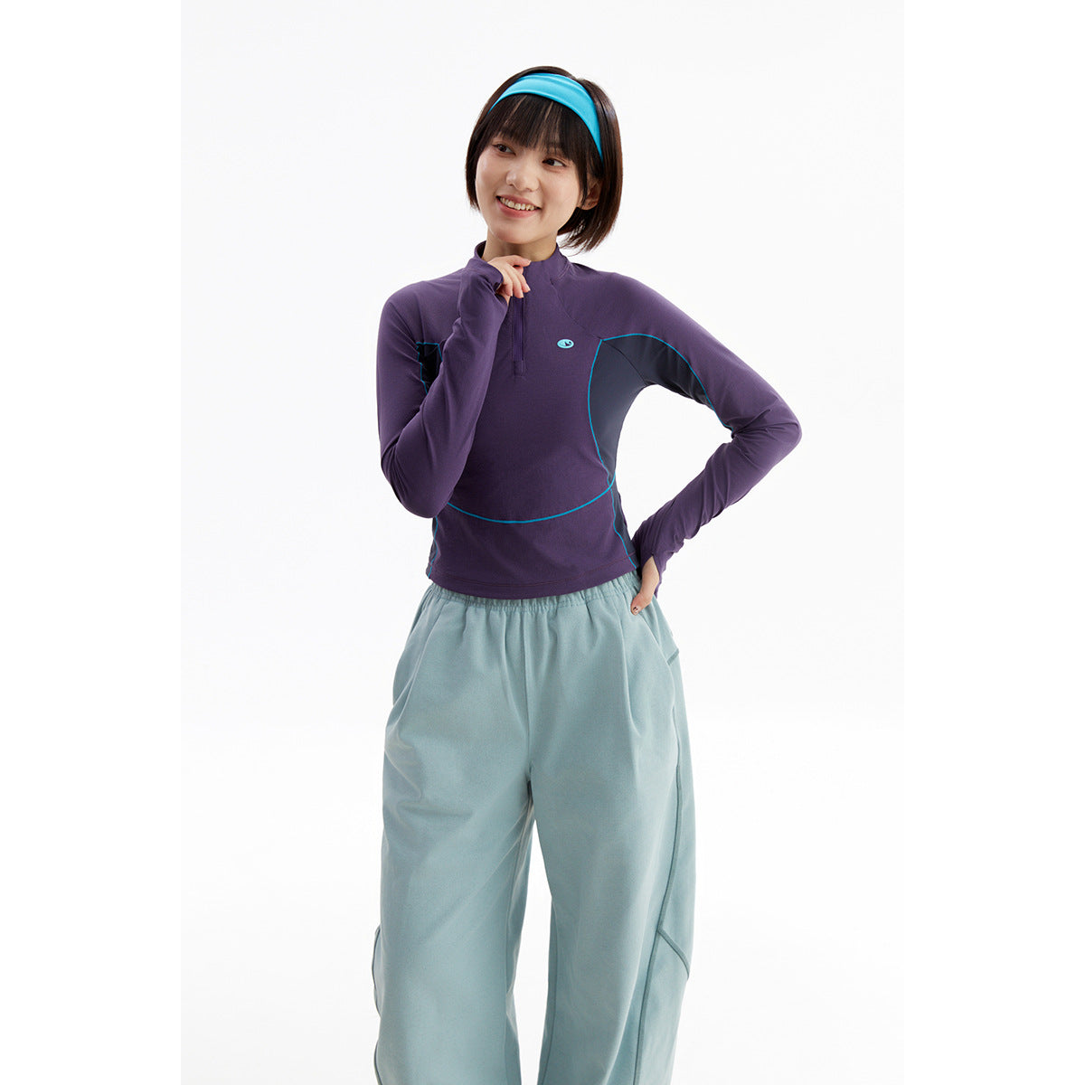 Model wearing a purple long-sleeve quarter-zip top with teal trim and loose pale blue pants.