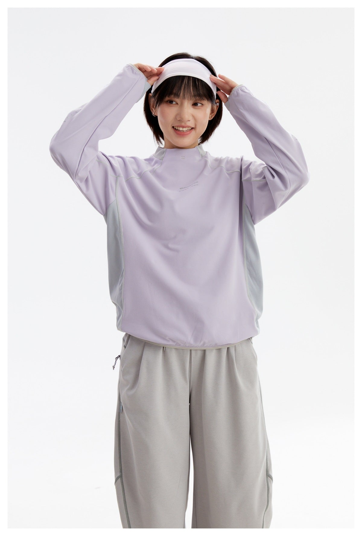 Model adjusts a white headband while wearing a lavender long-sleeve top with pale gray side panels and gray pants.